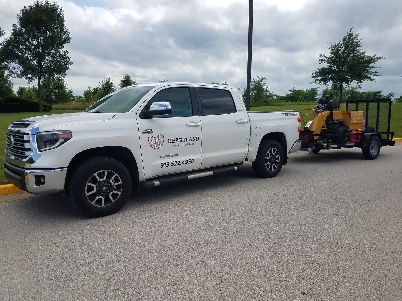 Heartland’s branded white truck with its yellow stump grinder loaded on a trailer