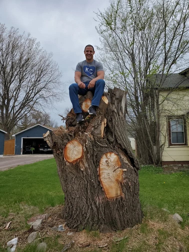 Matt Altrich sitting on a large cut tree trunk in a yard
